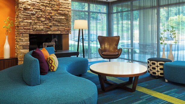 Un salon moderne avec une cheminée en pierre, un ensemble de canapés bleus, une table basse ronde et de grandes fenêtres donnant sur l’extérieur.