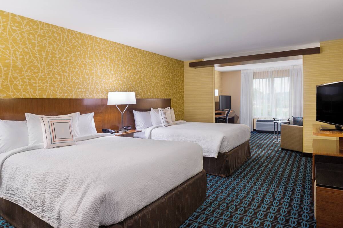 A hotel room with two beds, a desk with a TV, and a view of the city through large windows.