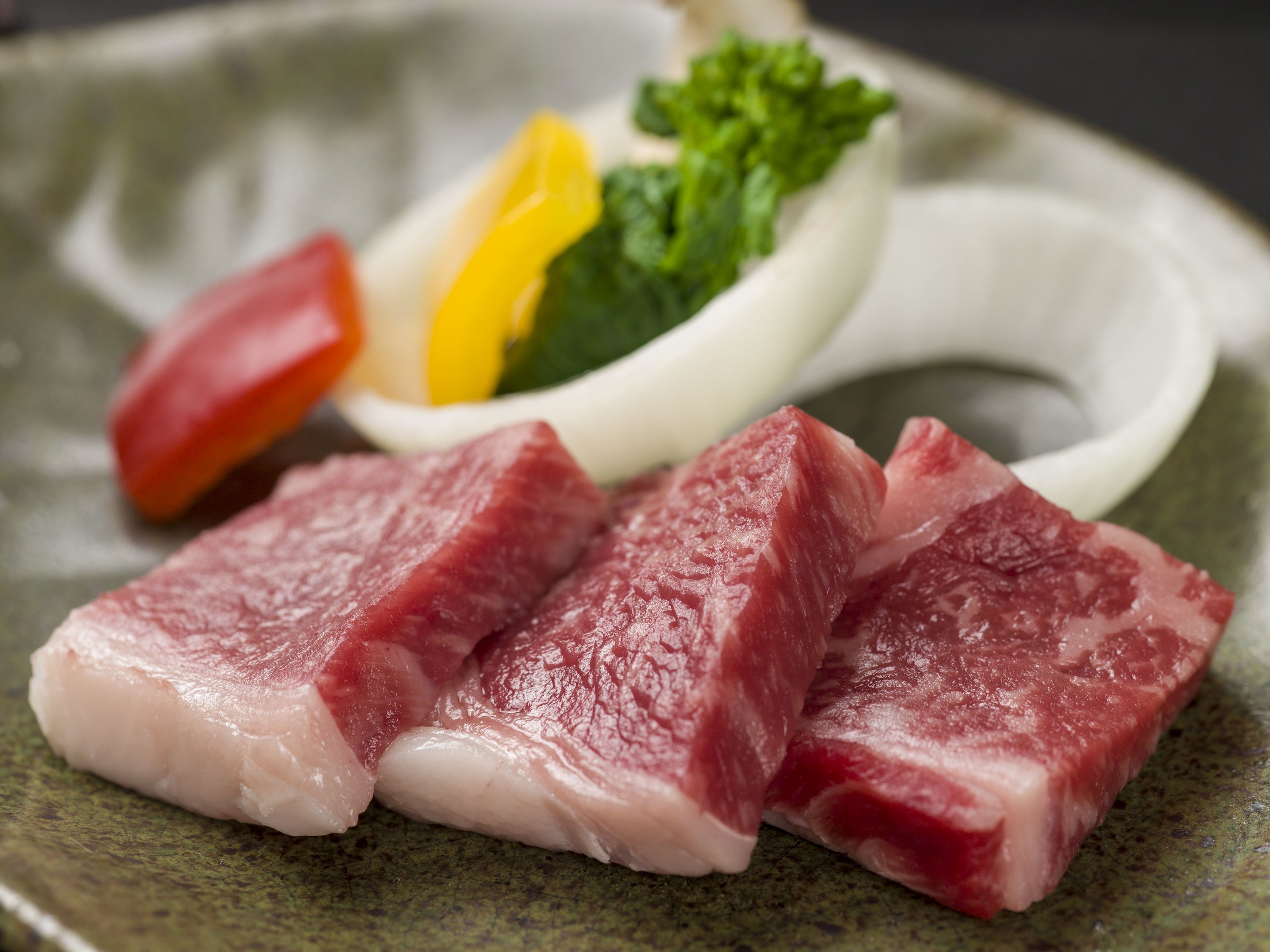 A plate with raw meat, vegetables, and a white bowl.