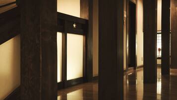 A corridor with wooden columns and a polished floor, leading to a door with frosted glass panels.