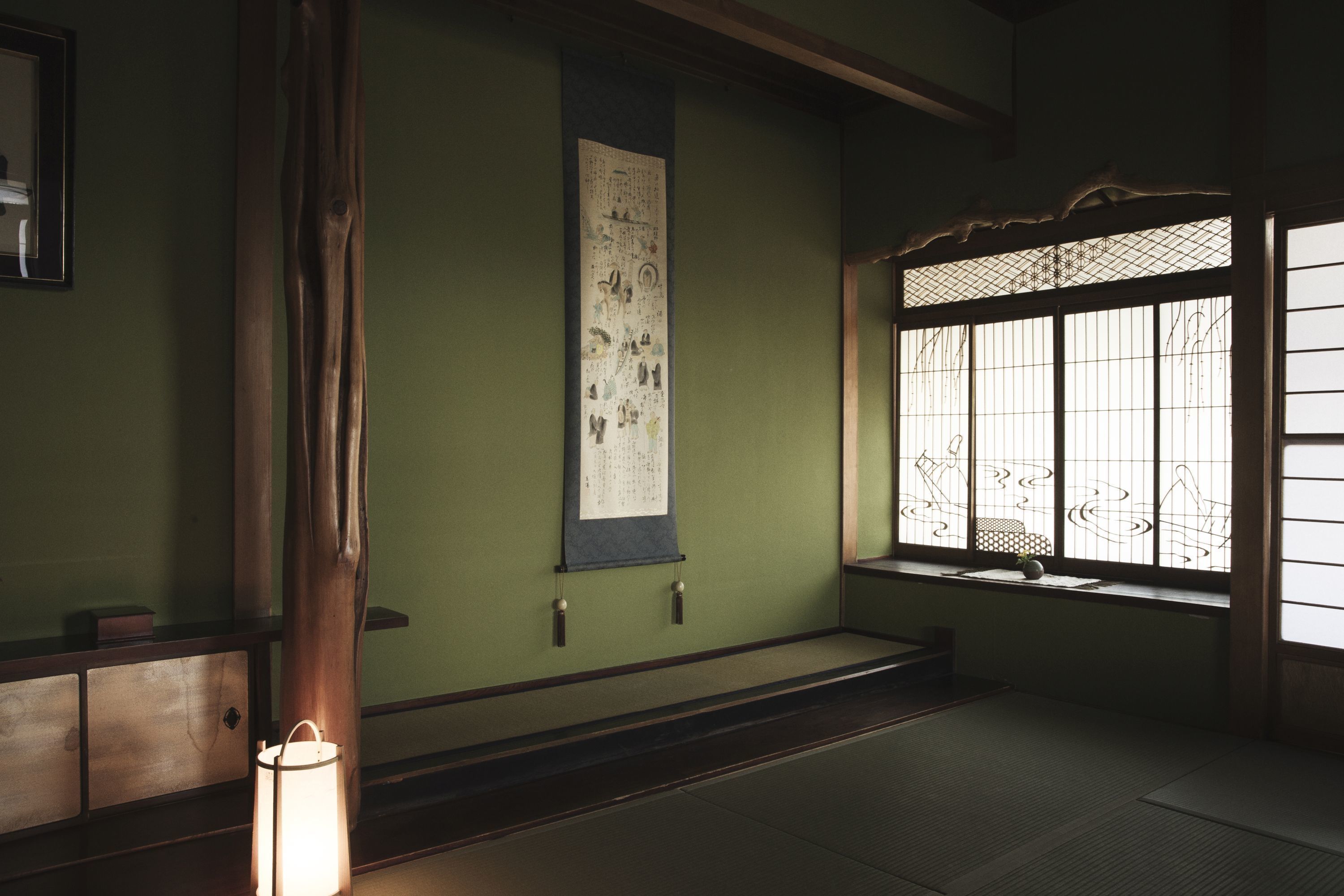 Una habitación japonesa tradicional con suelo de tatami, una pantalla shoji y un pergamino colgante.