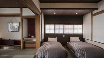 A traditional Japanese room with tatami flooring, two beds with striped bedding, a shoji screen window, and a small desk with a chair.
