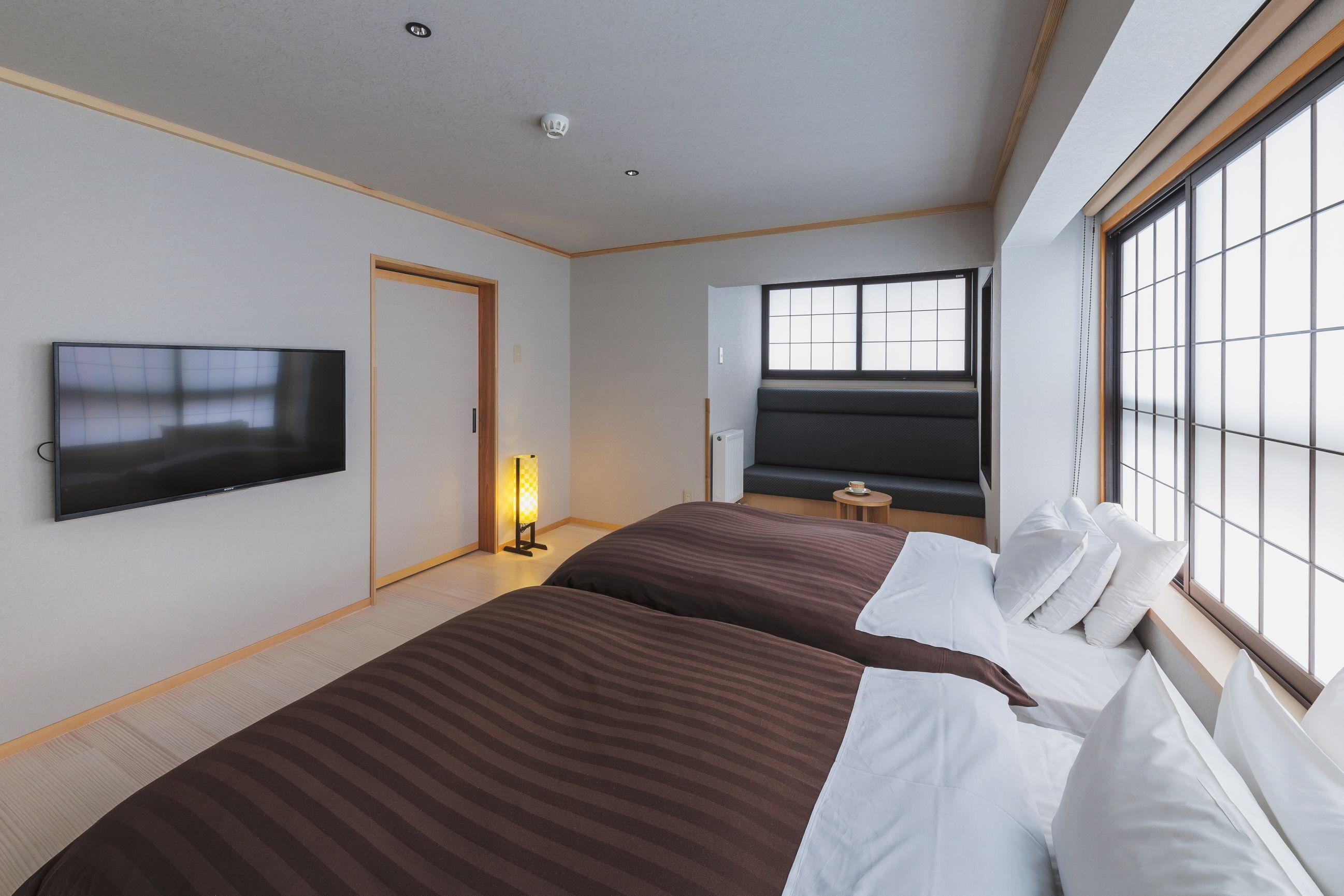 Una habitación de hotel con dos camas, un televisor de pantalla plana, un ventanal con vistas y una mesita de noche con lámpara.