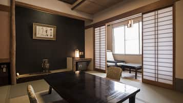 A traditional Japanese room with tatami flooring, a low table, a chair, a shoji screen, and a framed calligraphy piece on the wall.