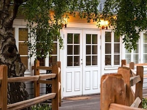 A wooden deck leading to a white door with glass panels, surrounded by trees. - The Lodge (Genarp)