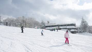 A snowy ski slope with skiers and a building in the background.