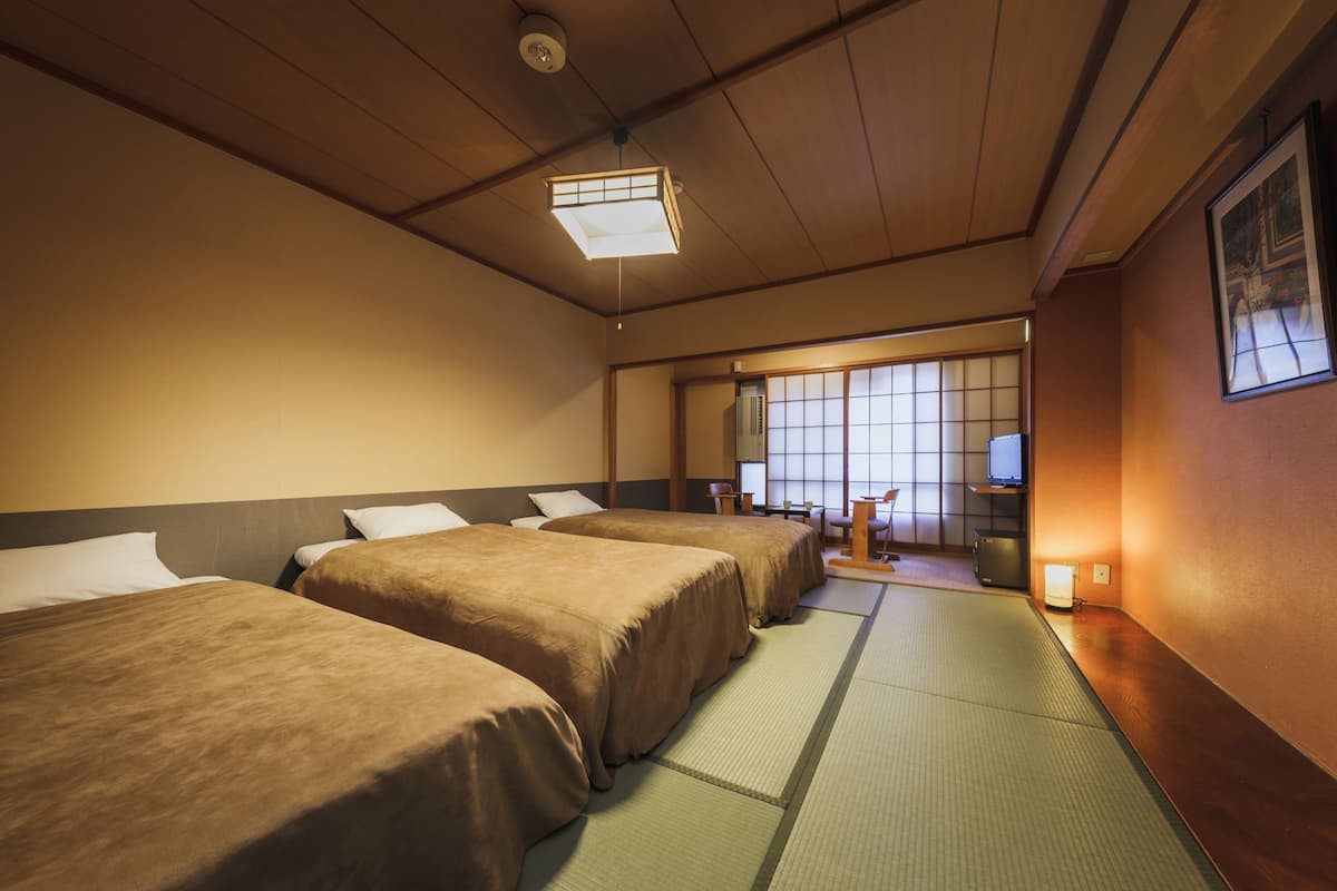 A hotel room with three beds, tatami mats, a traditional Japanese sliding door, and a television.