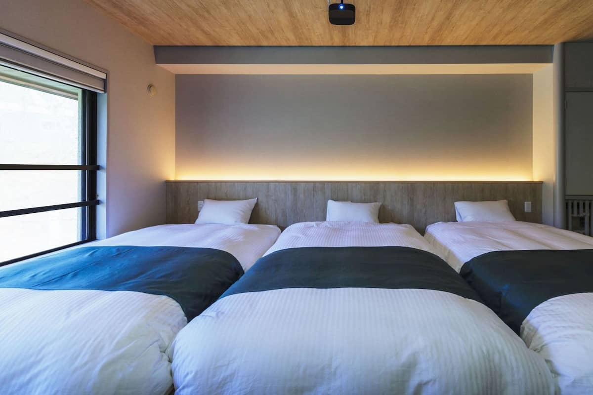 A hotel room with three beds, a wooden ceiling, and a view of the outside.