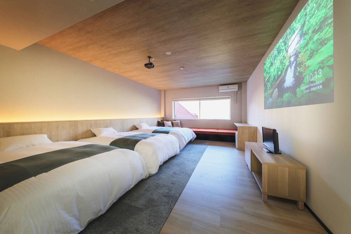 A modern hotel room with a large bed, a TV, and a projection screen displaying a nature scene.