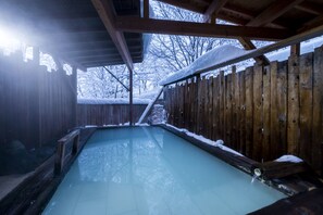 Un bain à remous en bois, doté d’une enceinte en verre, entouré d’une clôture en bois et recouvert de neige.