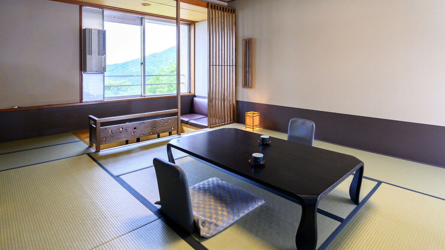 Ein traditioneller Tatami-Raum mit niedrigem Tisch, Stühlen, einer Bank und Blick auf einen Berg.