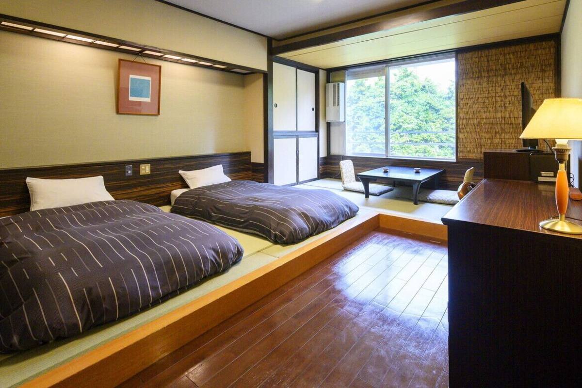 A hotel room with two beds, a desk, a chair, a lamp, and a window with a view.