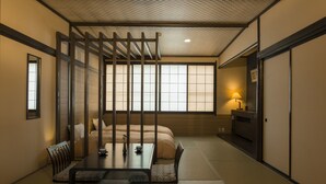 A traditional Japanese-style room with tatami flooring, a low table with cushions, a bed with a wooden headboard, and sliding doors. - Hotel Lucent Takamiya (Yamagata)