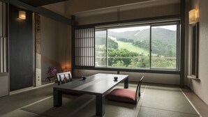 A traditional Japanese room with tatami flooring, a low table, a cushion, a sliding door, and a view of a green landscape. - Hotel Lucent Takamiya (Yamagata)
