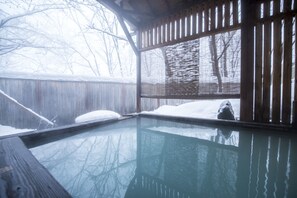 Un jacuzzi en verre, avec une terrasse en bois et une vue sur un jardin enneigé.