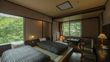 A hotel room with two beds, a desk, and a chair. There is a window with a view of trees.