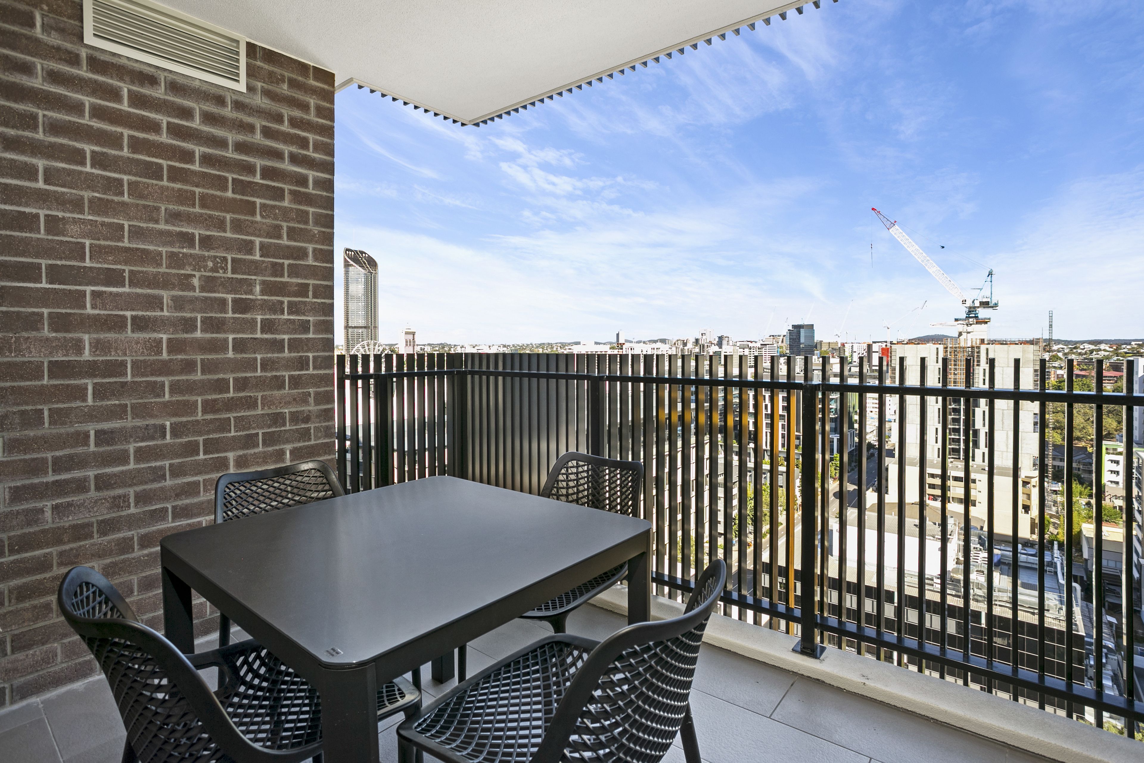 Un balcon avec une table et des chaises, un mur de briques et une vue sur le paysage urbain, avec des grues de construction en arrière-plan.