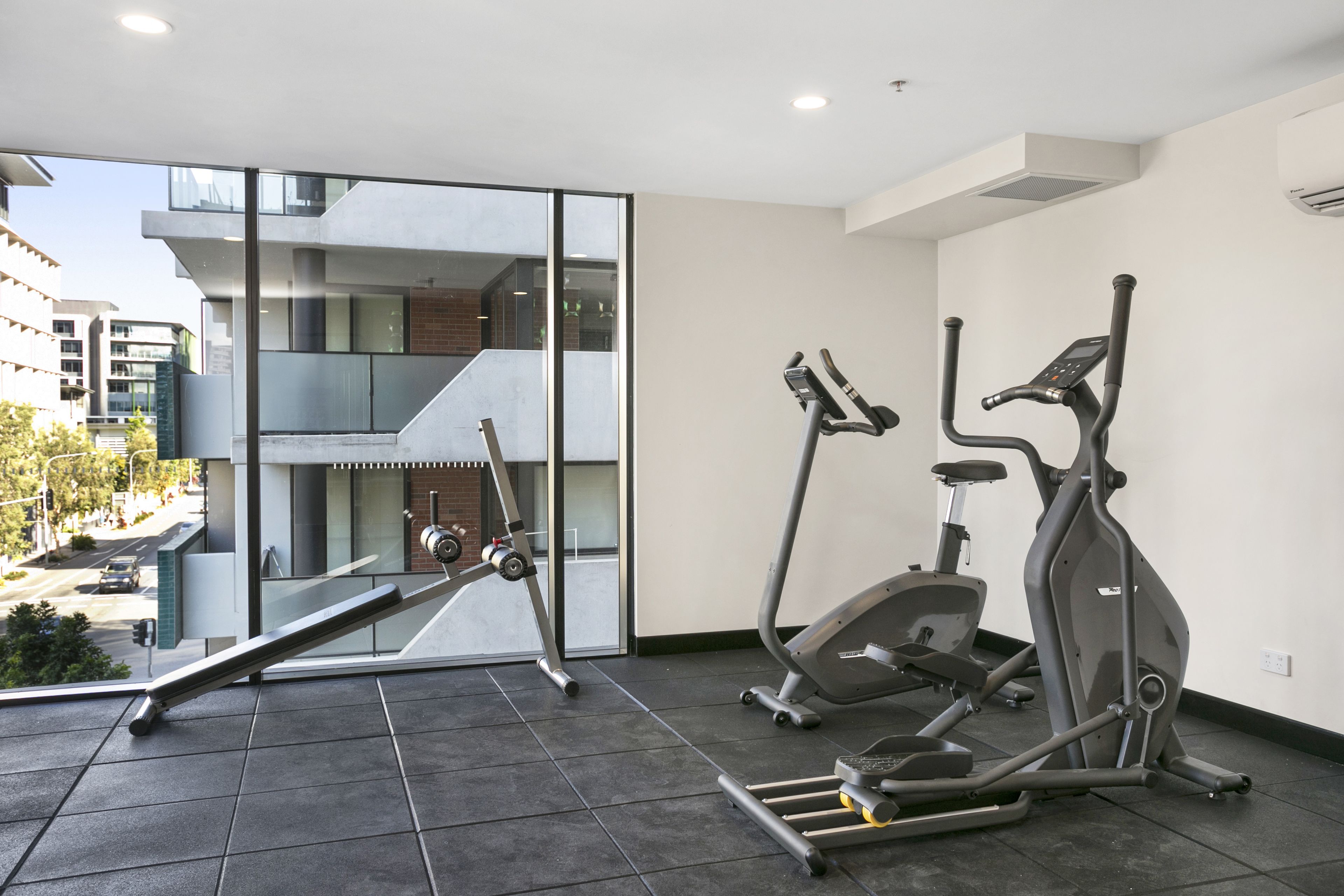 A modern gym with two stationary bikes and a treadmill, large windows offering a view of the city.