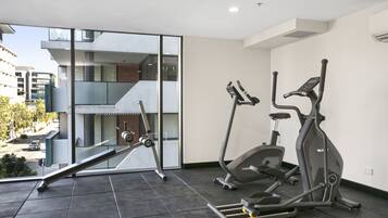A modern gym with two stationary bikes and a treadmill, large windows offering a view of the city.