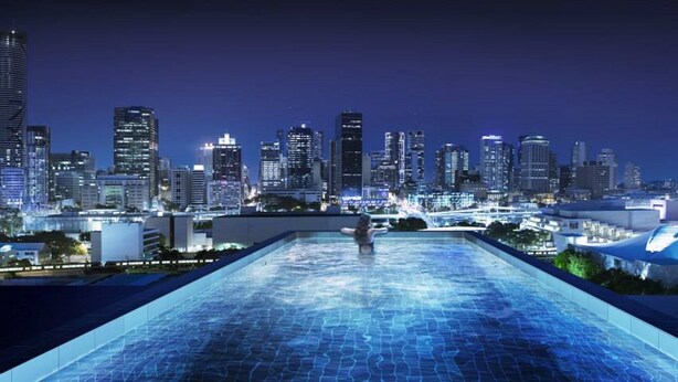 A rooftop infinity pool with a city skyline view at night. - Soda Apartments by CLLIX (South Brisbane)