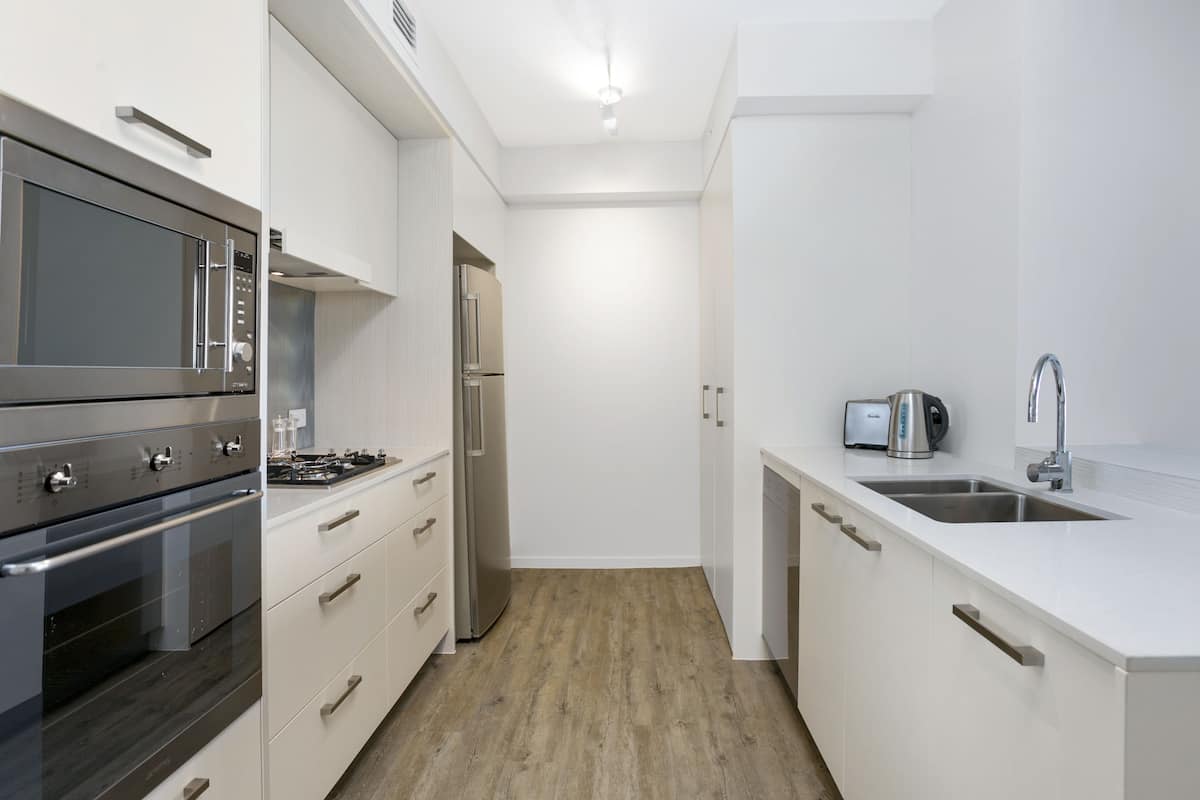 A modern kitchen with stainless steel appliances, white cabinetry, and a wooden floor.