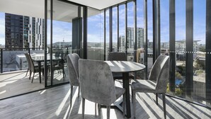 A modern dining area with a round table and four chairs, large floor-to-ceiling windows, and a view of the cityscape. - Soda Apartments by CLLIX (South Brisbane)