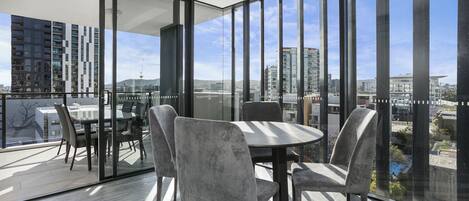 A modern dining area with a round table and four chairs, large floor-to-ceiling windows, and a view of the cityscape.