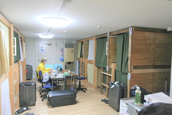 Una habitación con paredes de madera, un escritorio, sillas y una computadora. Hay maletas y una botella en el suelo.