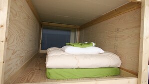 A small wooden room with a bed, a window with blinds, and a slanted ceiling. - Edo Tokyo Hostel (Tokyo)