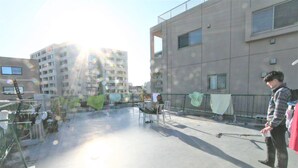 A rooftop terrace with a view of adjacent buildings, metal railings, and a person standing. - Edo Tokyo Hostel (Tokyo)