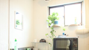 A compact kitchen with a wooden table, a microwave, and a window with a plant. - Edo Tokyo Hostel (Tokyo)