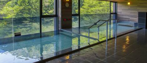 A modern indoor swimming pool with glass walls, a wooden ceiling, and a digital clock.