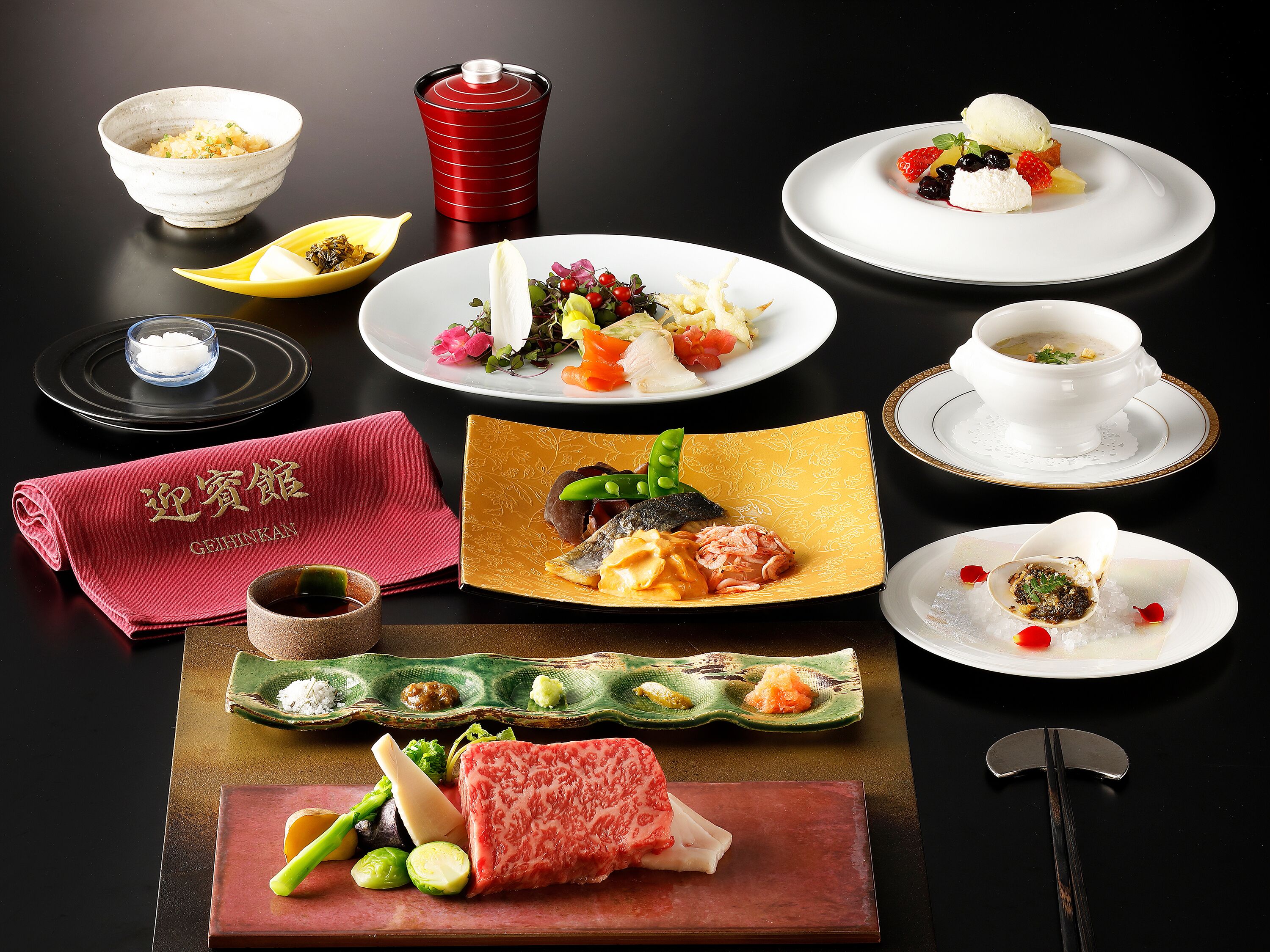 A variety of Japanese dishes including sushi, sashimi, and a bowl of soup, arranged on a black table.