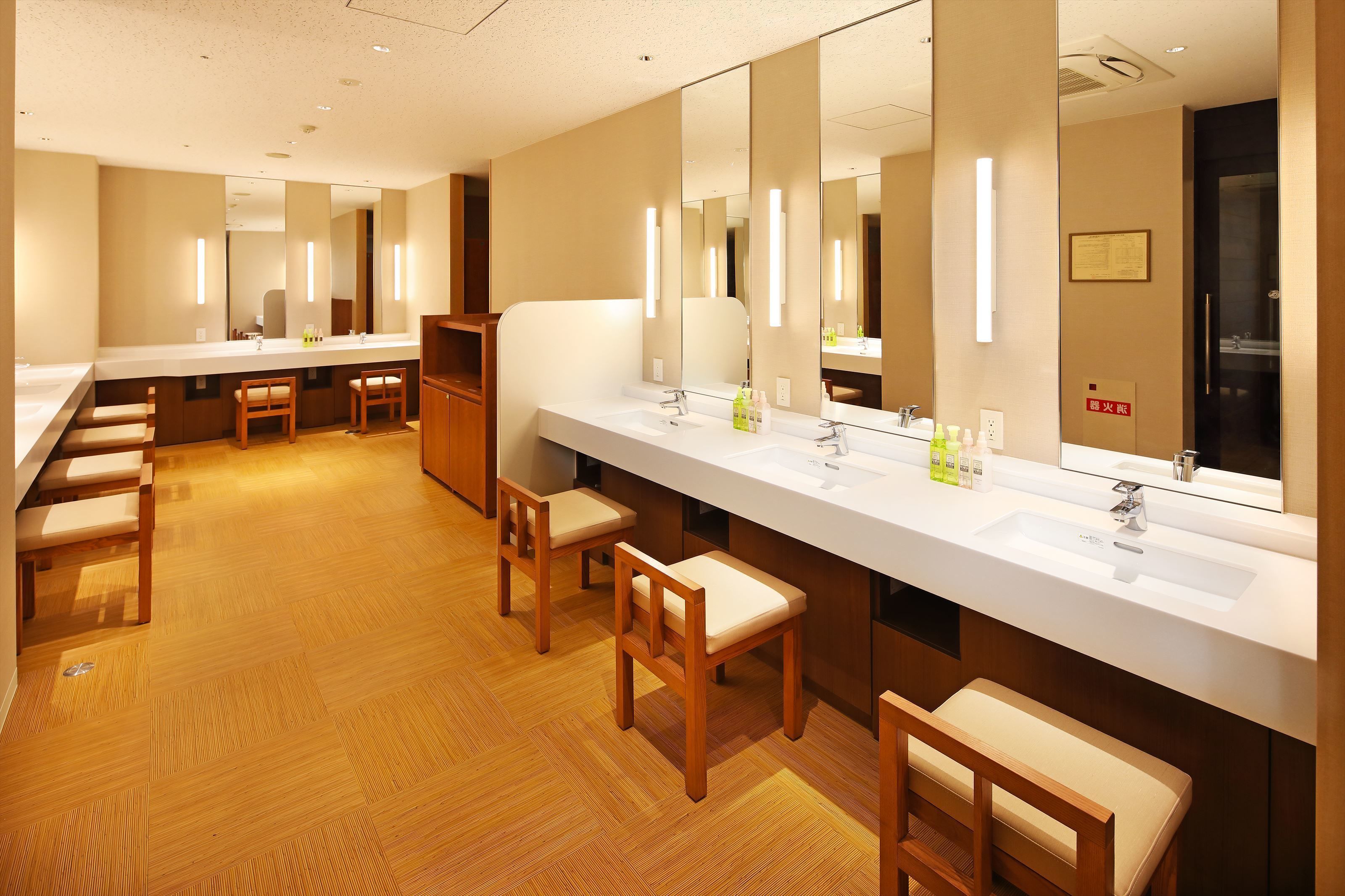 A hotel bathroom with multiple sinks, mirrors, and wooden chairs.