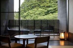 Um interior moderno com uma mesa redonda e cadeiras, um banco e vista para vegetação exuberante através de amplas janelas.