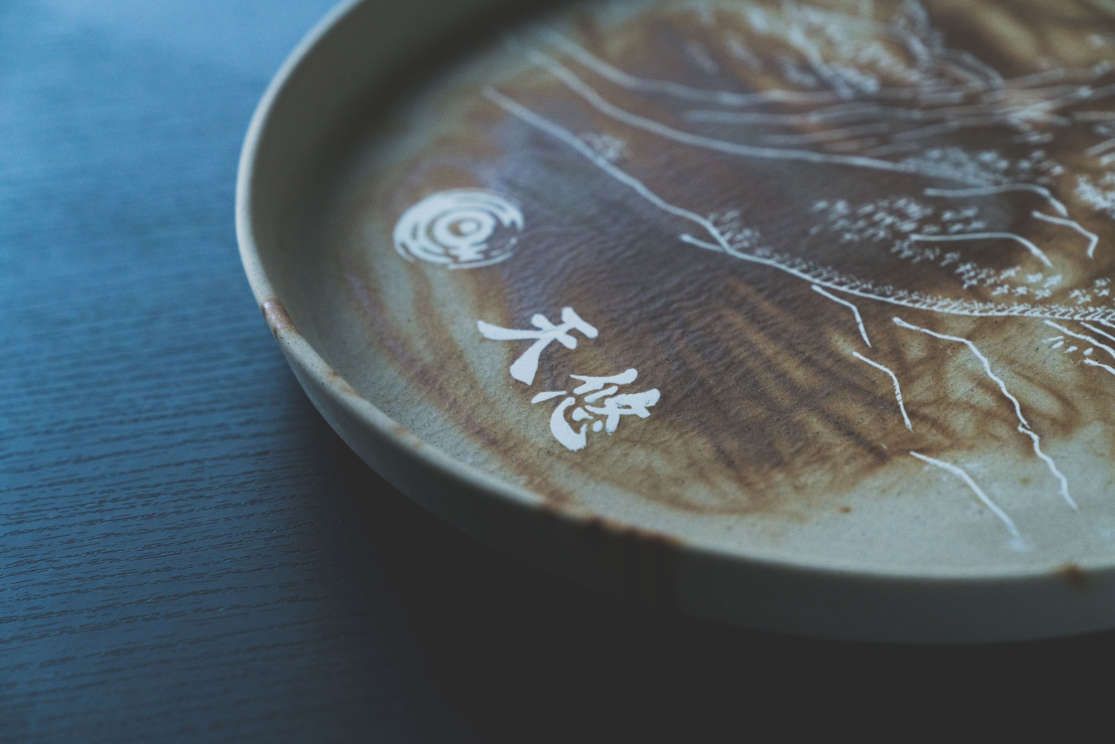 A close-up of a ceramic plate with intricate white designs and Japanese characters.