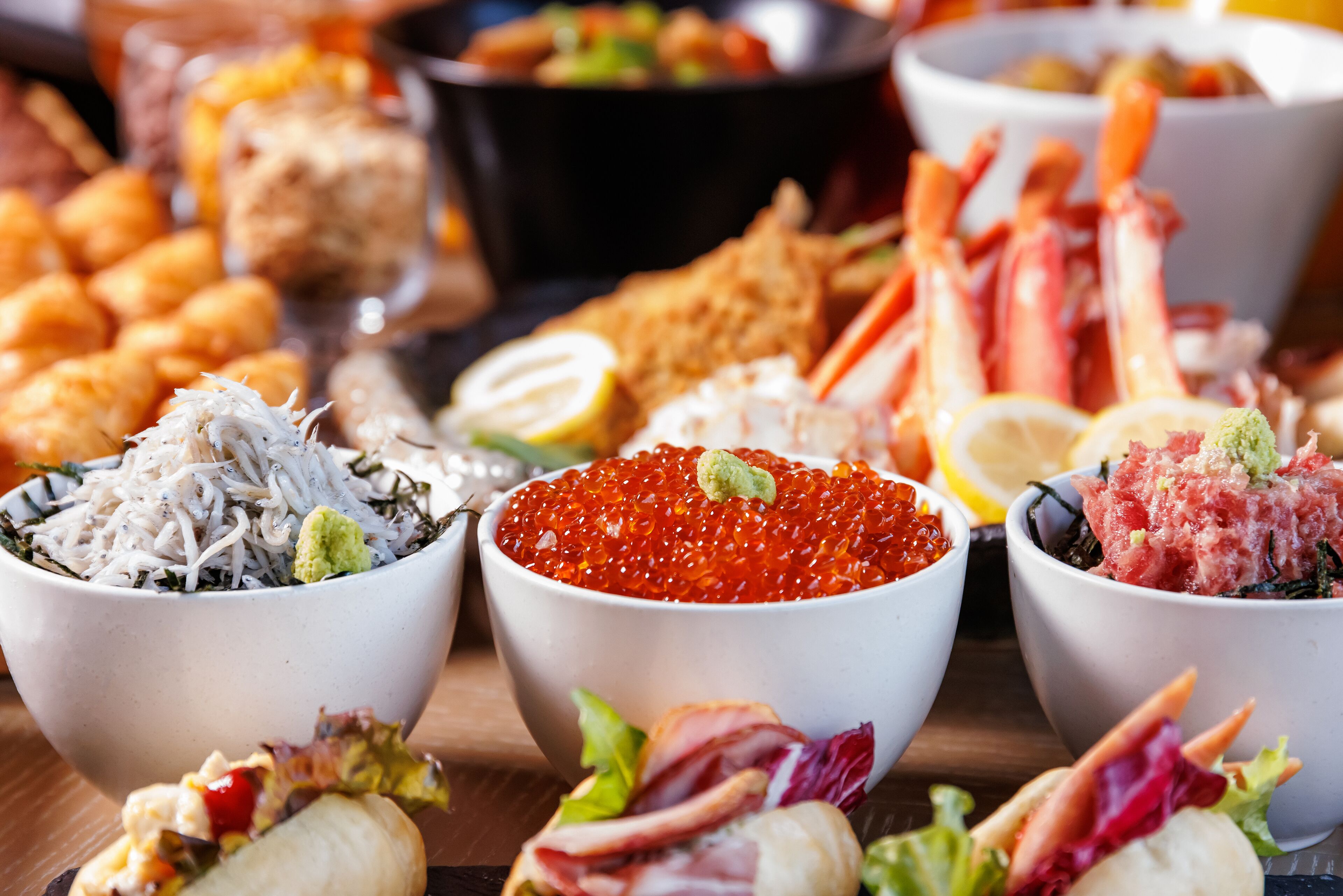 A variety of food items including bowls of seaweed salad, red caviar, and other seafood delicacies.
