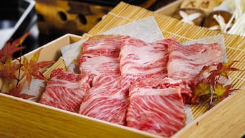 A wooden box filled with neatly arranged slices of red and white marbled meat, likely Wagyu beef, placed on a bamboo mat.