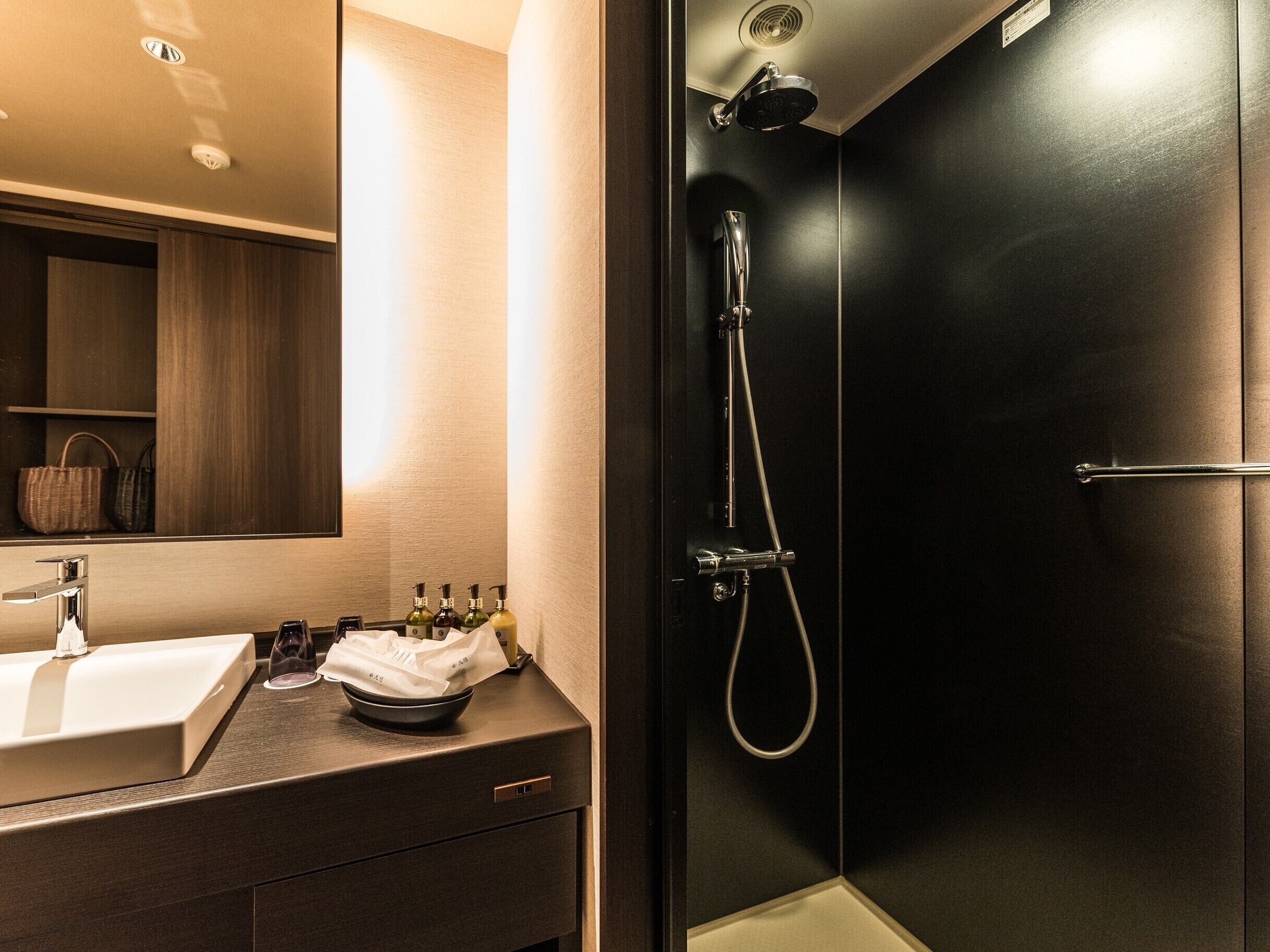 A modern bathroom with a dark-shaded shower enclosure, a sink with a mirror, and toiletries on the counter.