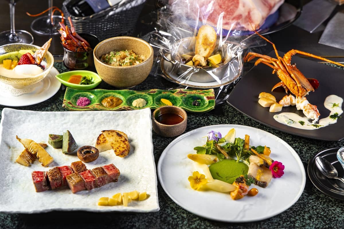 Diverse gerechten op een tafel, waaronder steak, kreeft en andere zeevruchten, met wijnglazen en een broodmand.