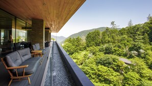 A modern outdoor seating area with a wooden ceiling, overlooking a lush forested hillside.