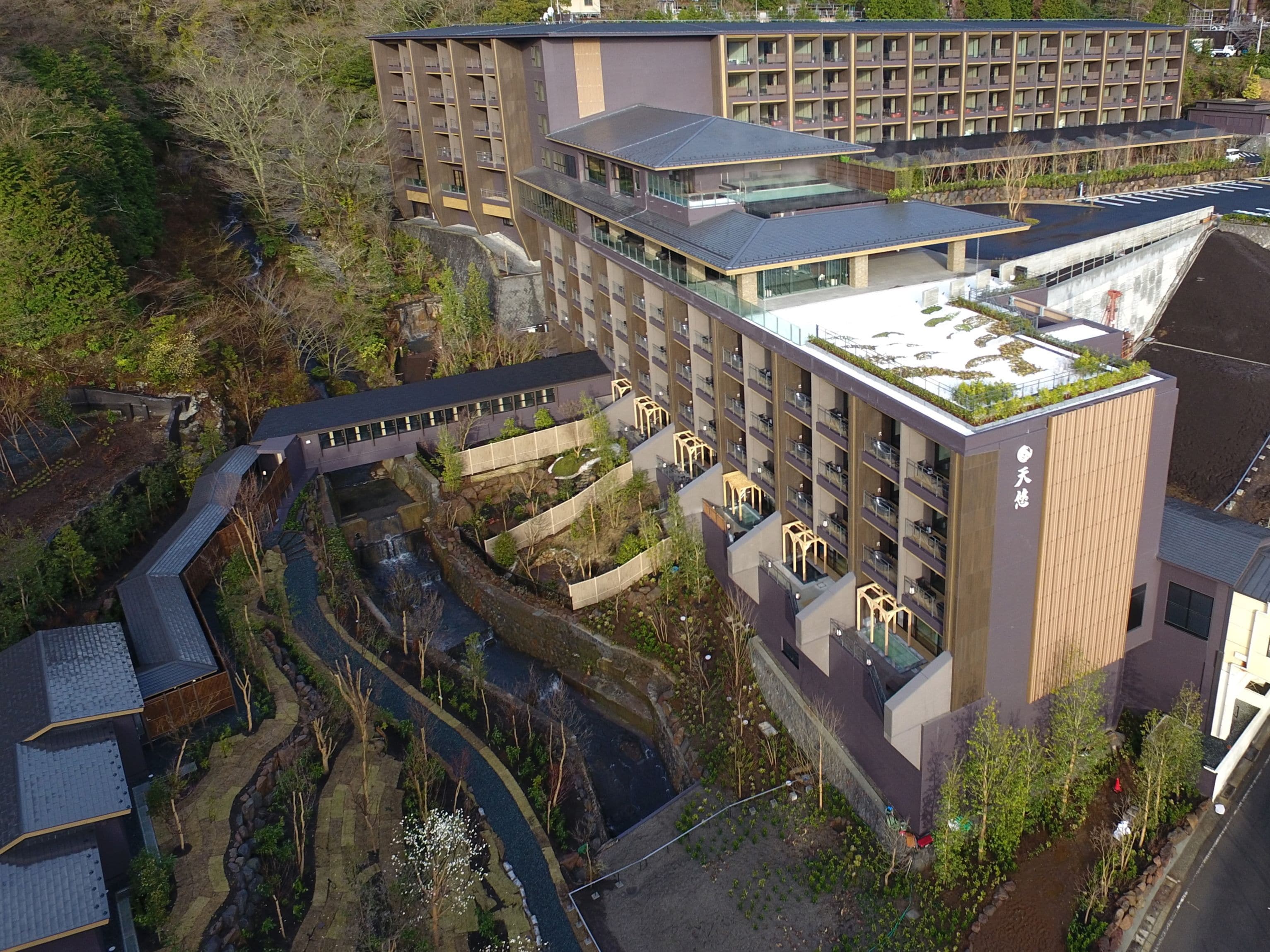 A modern hotel with multiple floors, a rooftop garden, and a small waterfall feature.