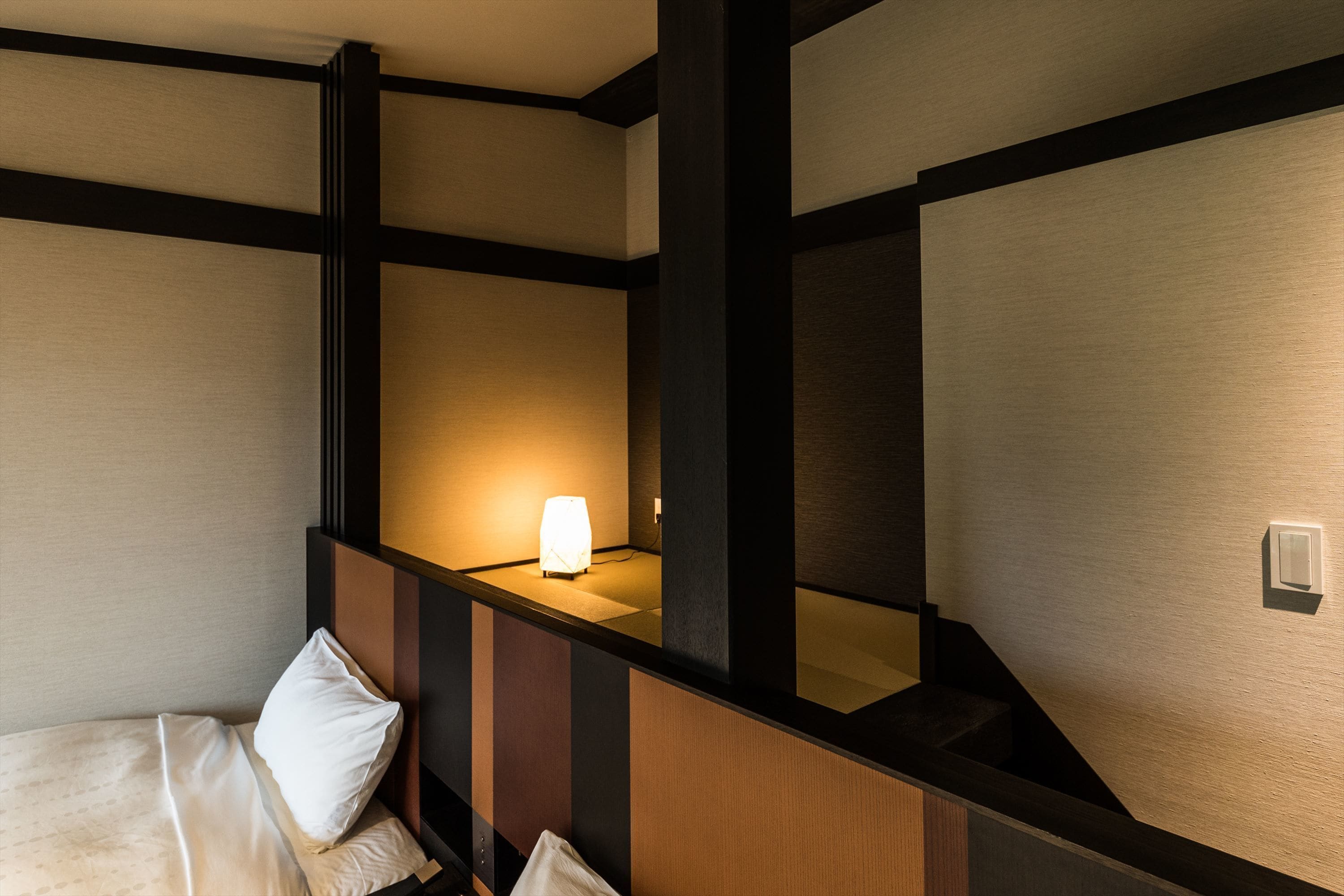 A hotel room with a bed, a nightstand, and a wall-mounted light.