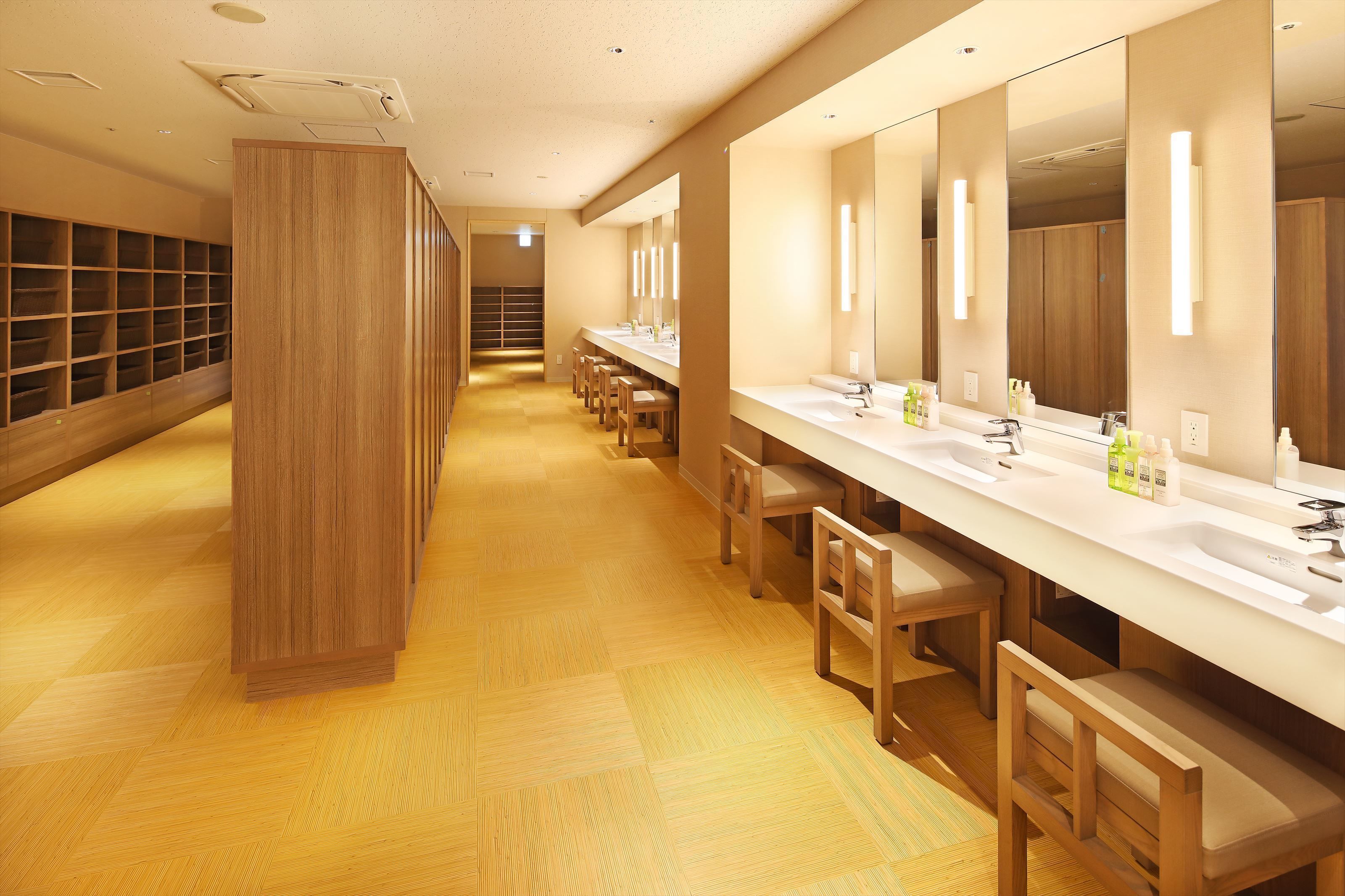 A modern bathroom with wooden flooring, multiple sinks, and a large mirror.