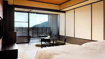 A hotel room with a bed, a desk, a chair, and a view of a balcony with a table and chairs.