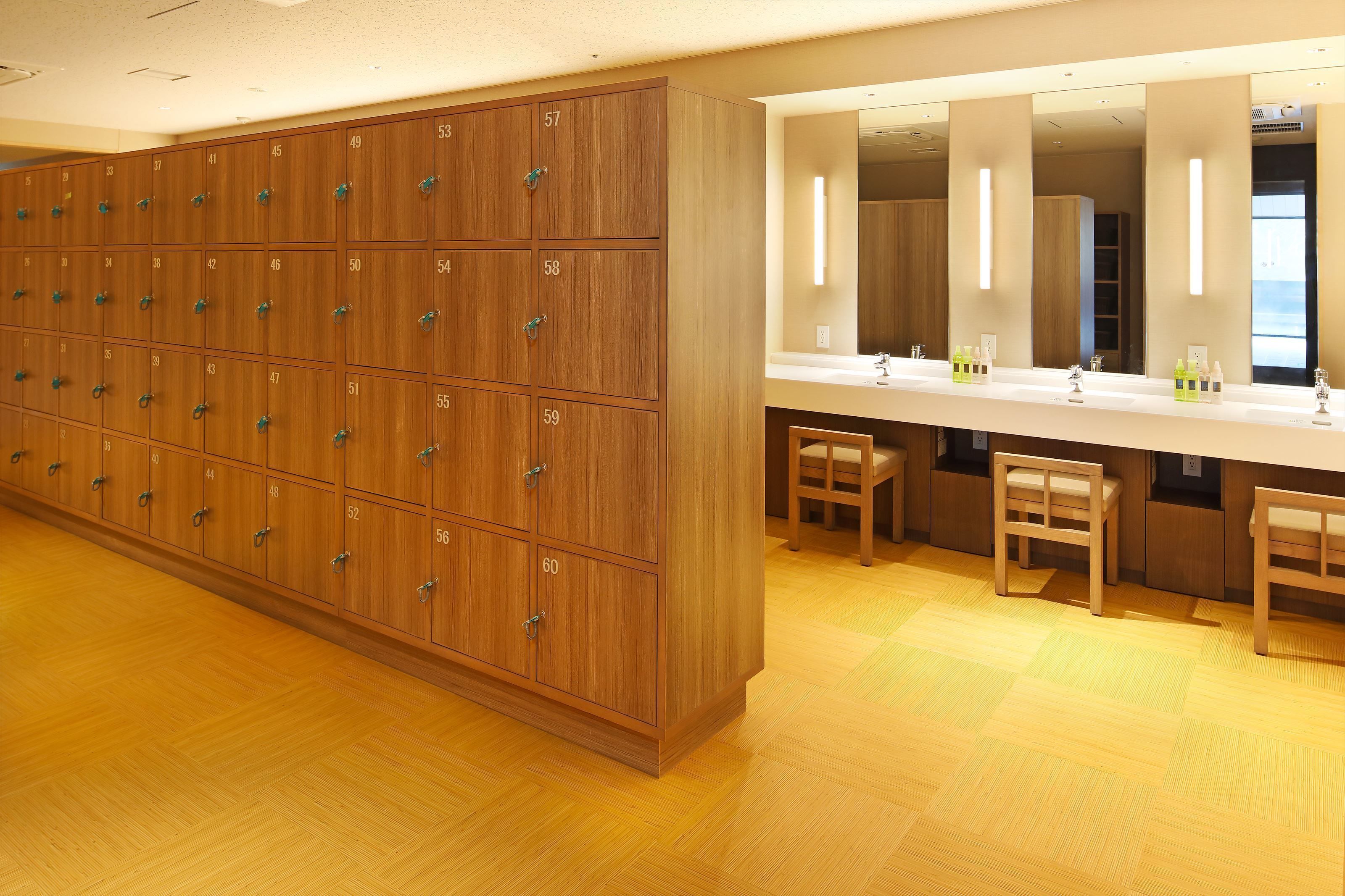 Una fila di armadietti in legno con numeri, un grande specchio e due sedie di legno in un bagno ben illuminato.
