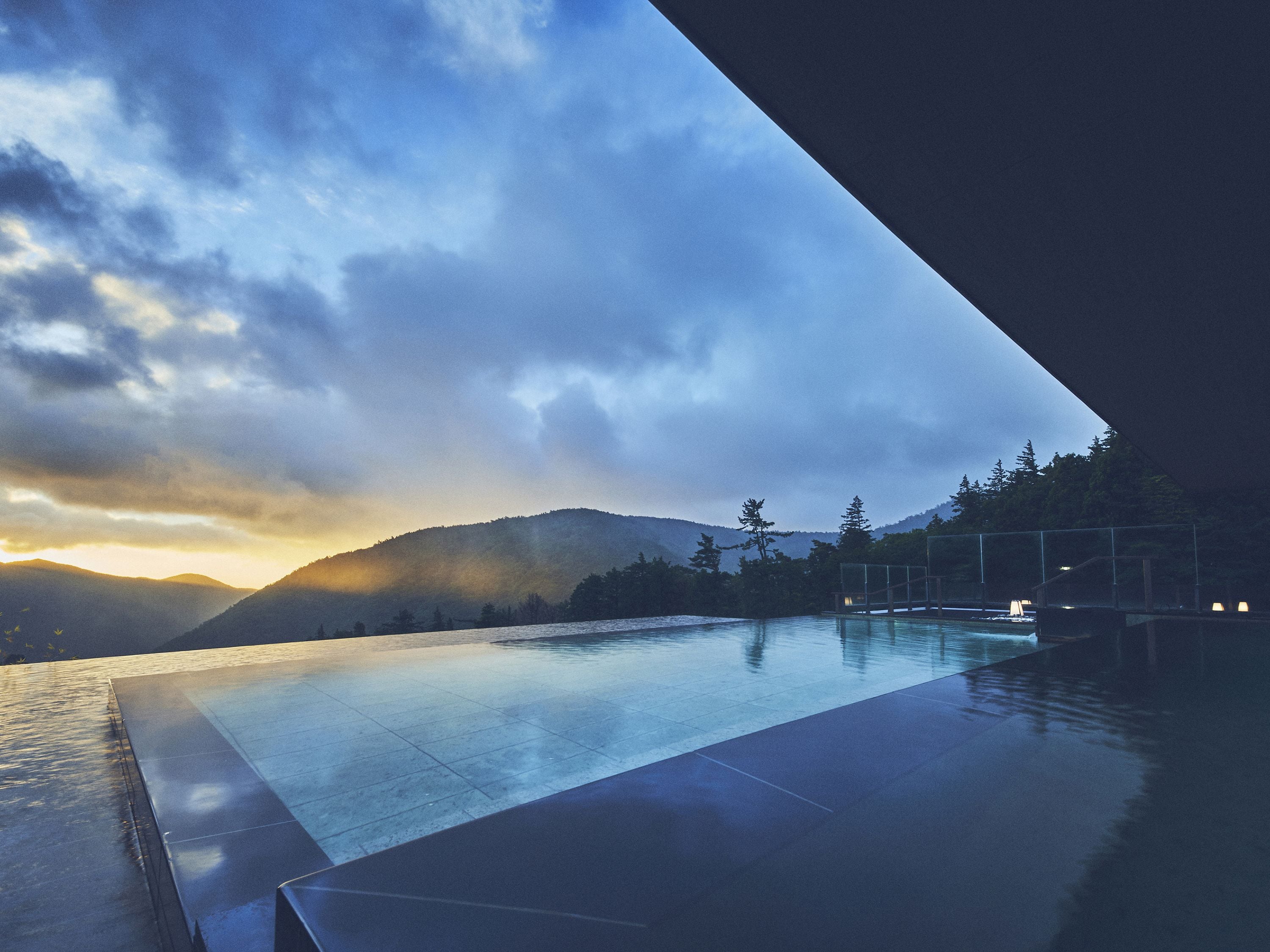 An infinity pool with a view of mountains and a sunset.