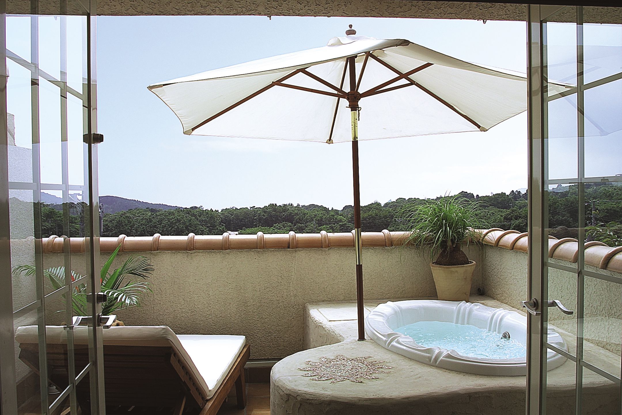 A balcony with a hot tub, a table, and an umbrella.