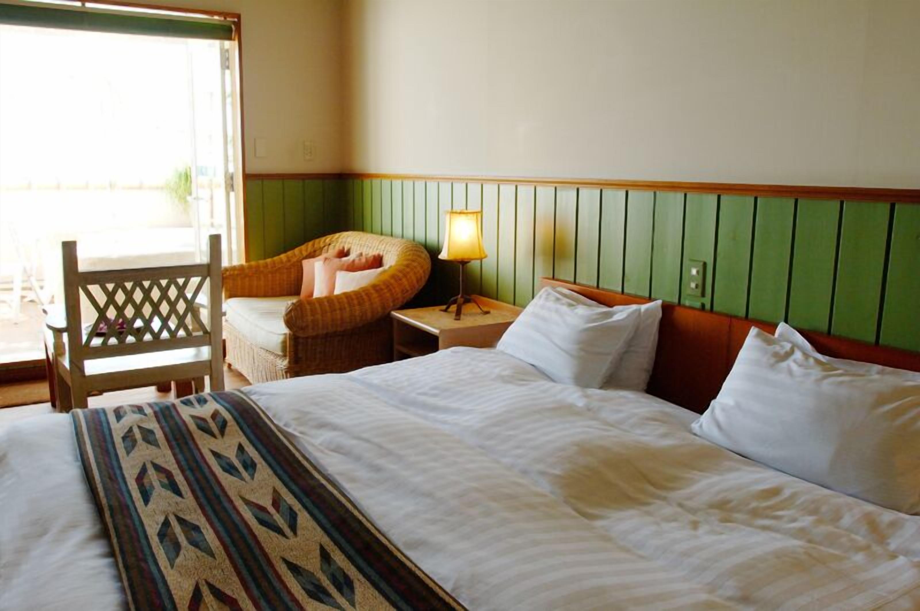 Une chambre d’hôtel avec un lit, une chaise, une lampe et une vue sur l’extérieur.