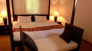 A four-poster bed with white linens, two bedside tables with lamps, and a view of greenery through the window.